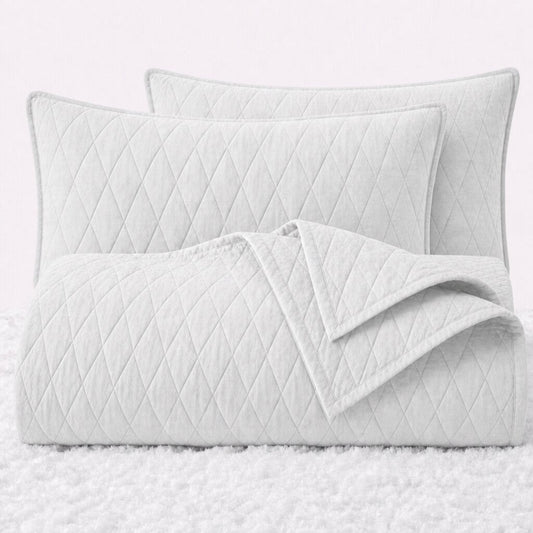 Folded white diamond quilted cover with two matching pillow shams on a white textured surface.