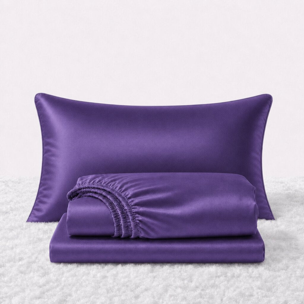 Folded shiny purple satin sheets in front of one matching pillow on a white textured surface.
