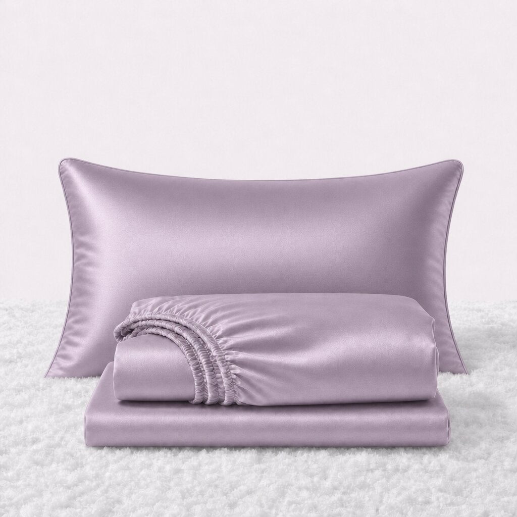 Folded shiny lavender satin sheets in front of one matching pillow on a white textured surface.