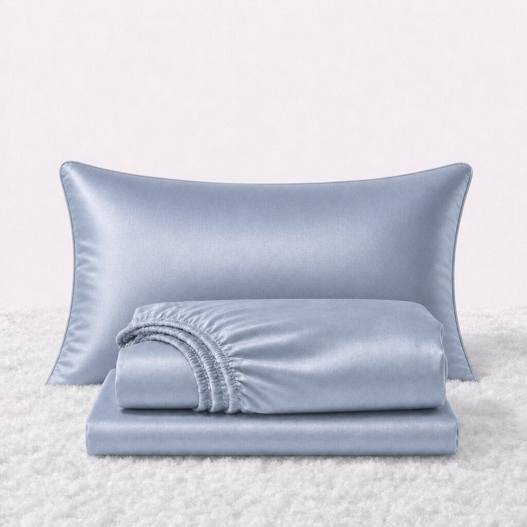 Folded shiny light blue satin sheets in front of one matching pillow on a white textured surface.