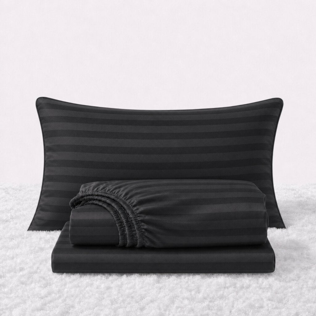 Folded shiny black striped satin sheets in front of one matching pillow on a white textured surface.