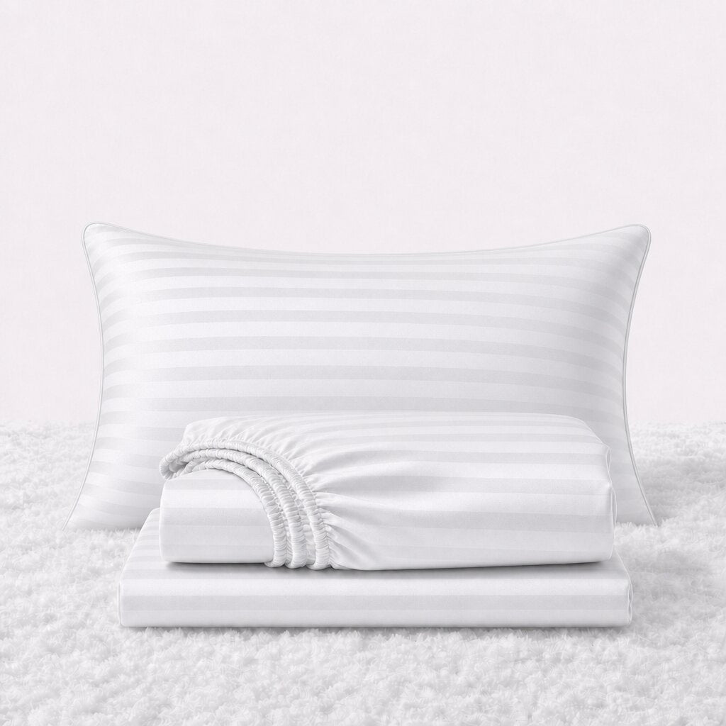 Folded shiny white striped satin sheets in front of one matching pillow on a white textured surface.