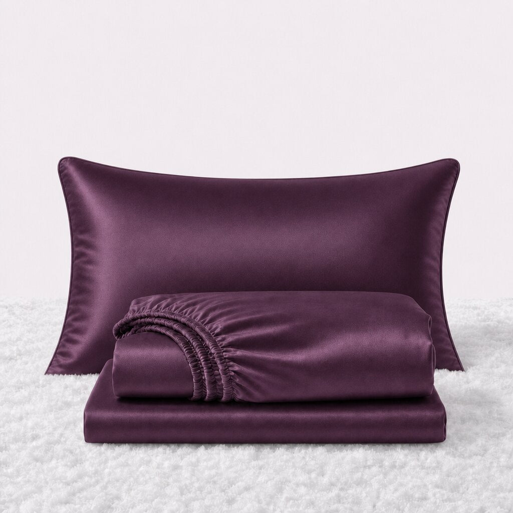 Folded shiny plum satin sheets in front of one matching pillow on a white textured surface.