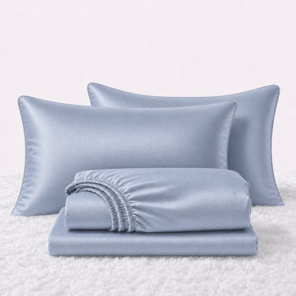 Folded shiny light blue satin sheets in front of two matching pillows on a white textured surface.