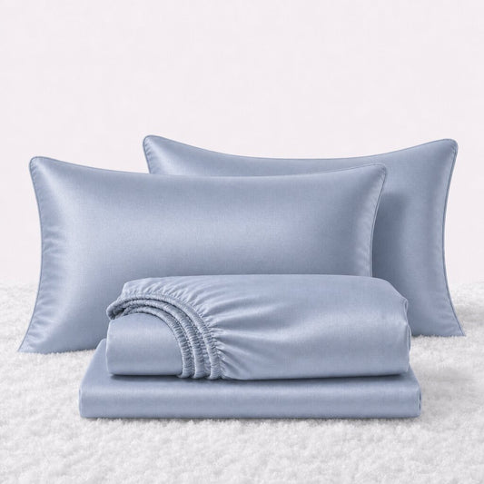 Folded shiny light blue satin sheets in front of two matching pillows on a white textured surface.