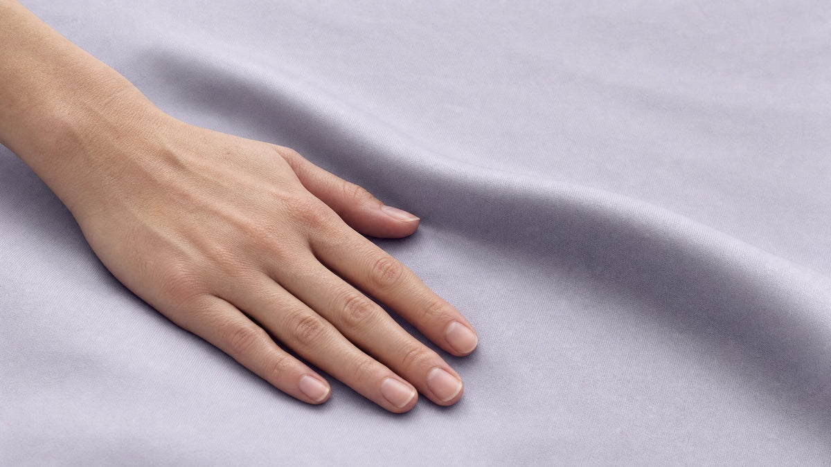 Close view of a hand resting on smooth pale lavender fabric.