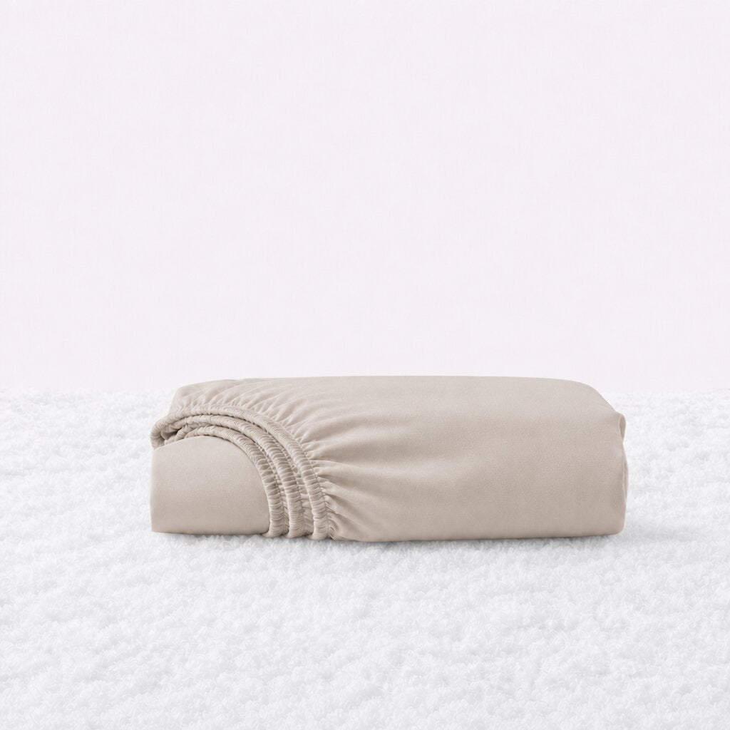 Folded beige fitted sheet with its gathered elastic edge visible on a white textured surface.