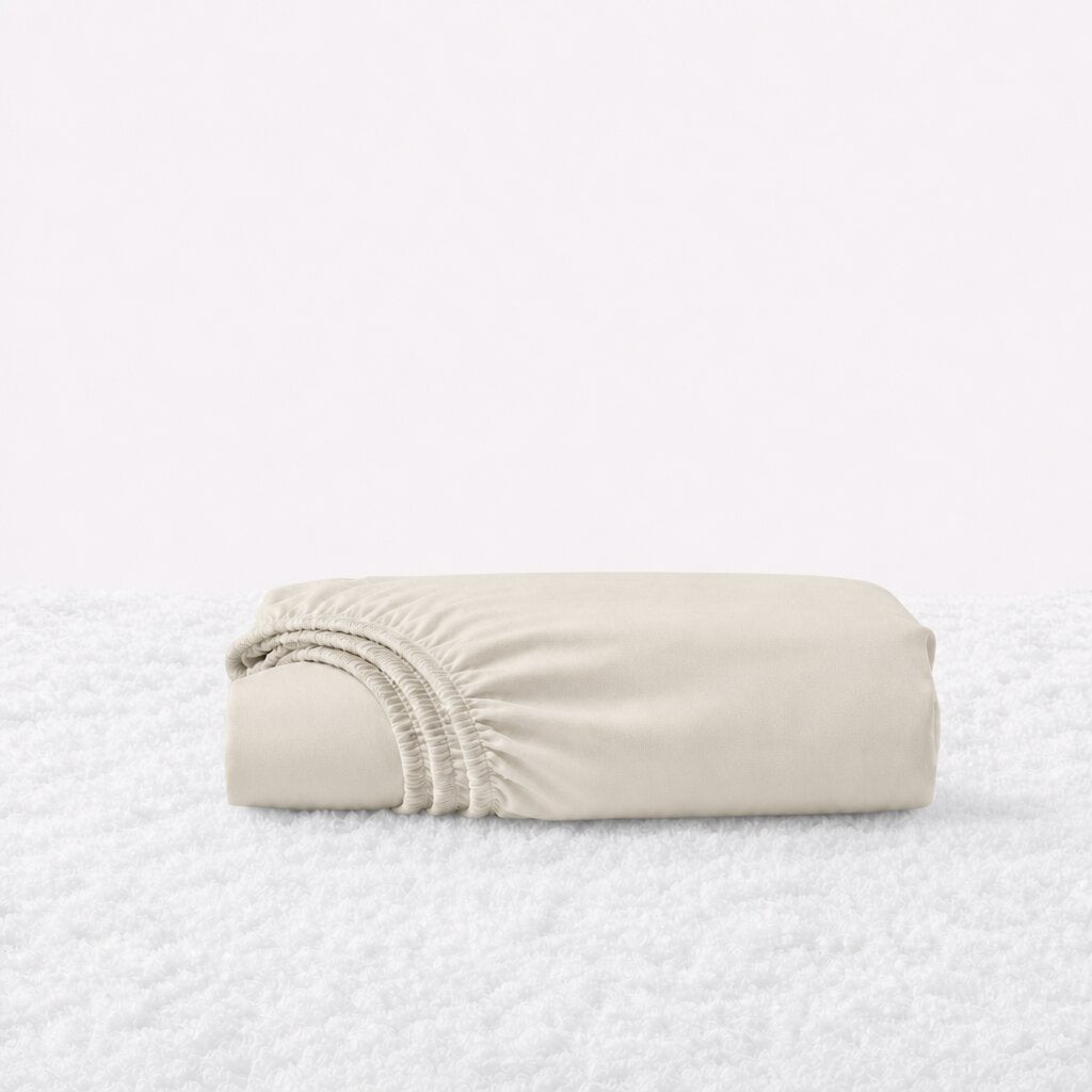 Folded cream fitted sheet with its gathered elastic edge visible on a white textured surface.