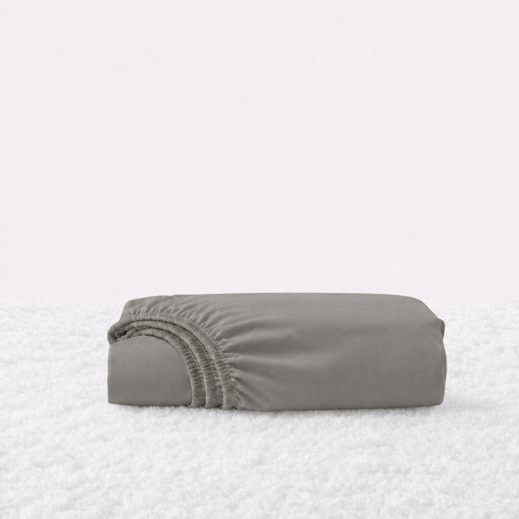 Folded warm gray fitted sheet with its gathered elastic edge visible on a white textured surface.