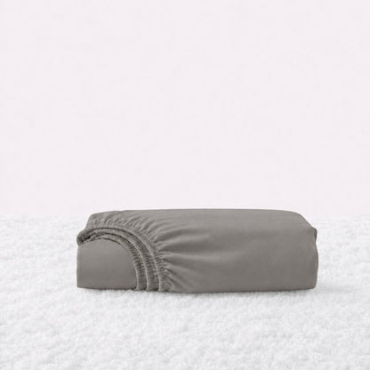 Folded warm gray fitted sheet with its gathered elastic edge visible on a white textured surface.
