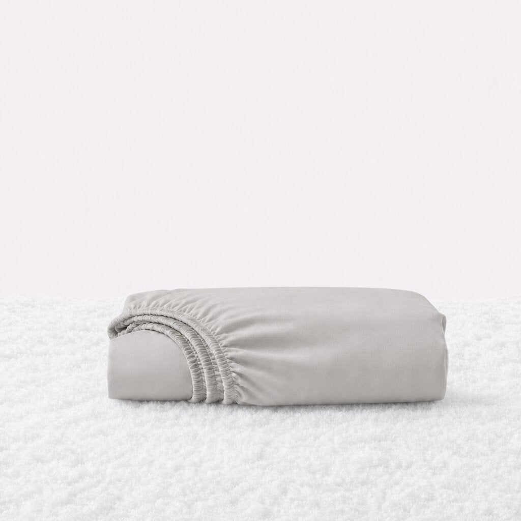 Folded light gray fitted sheet with its gathered elastic edge visible on a white textured surface.