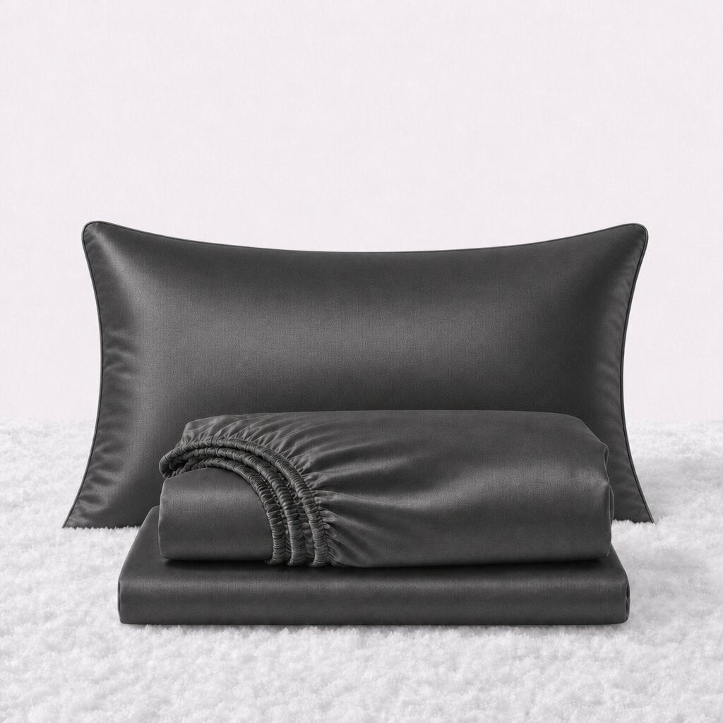Folded shiny black satin sheets in front of one matching pillow on a white textured surface.