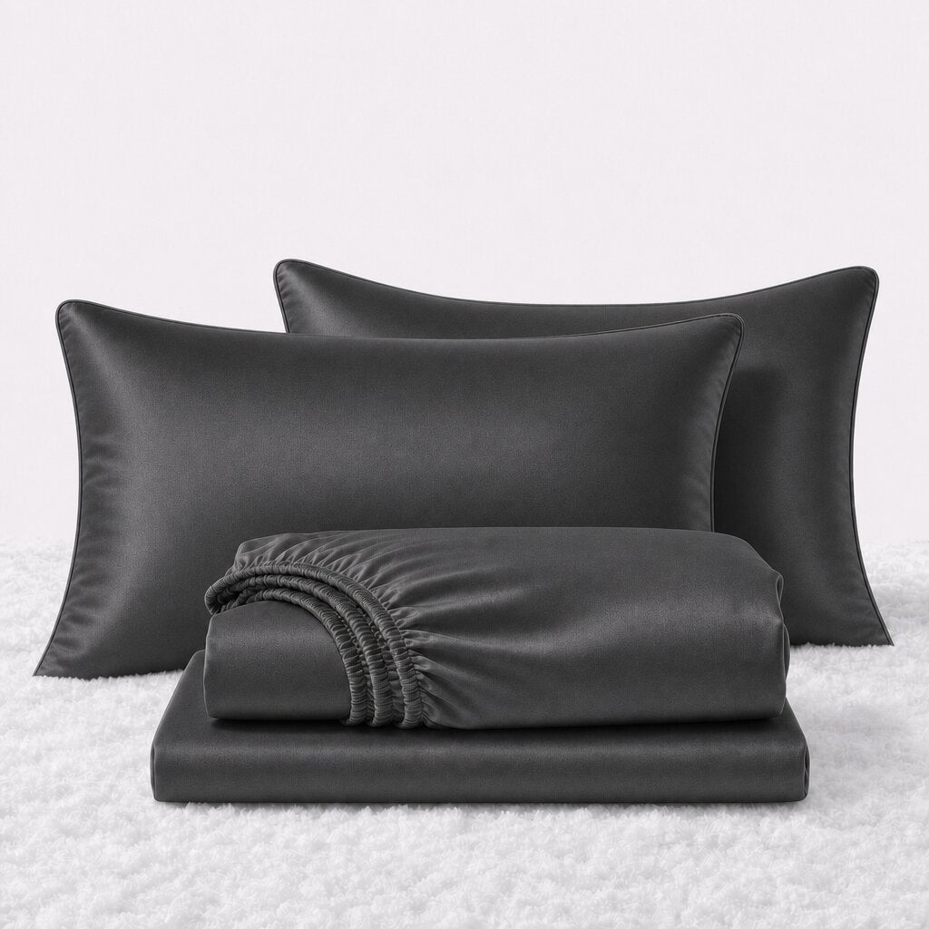 Folded shiny black satin sheets in front of two matching pillows on a white textured surface.