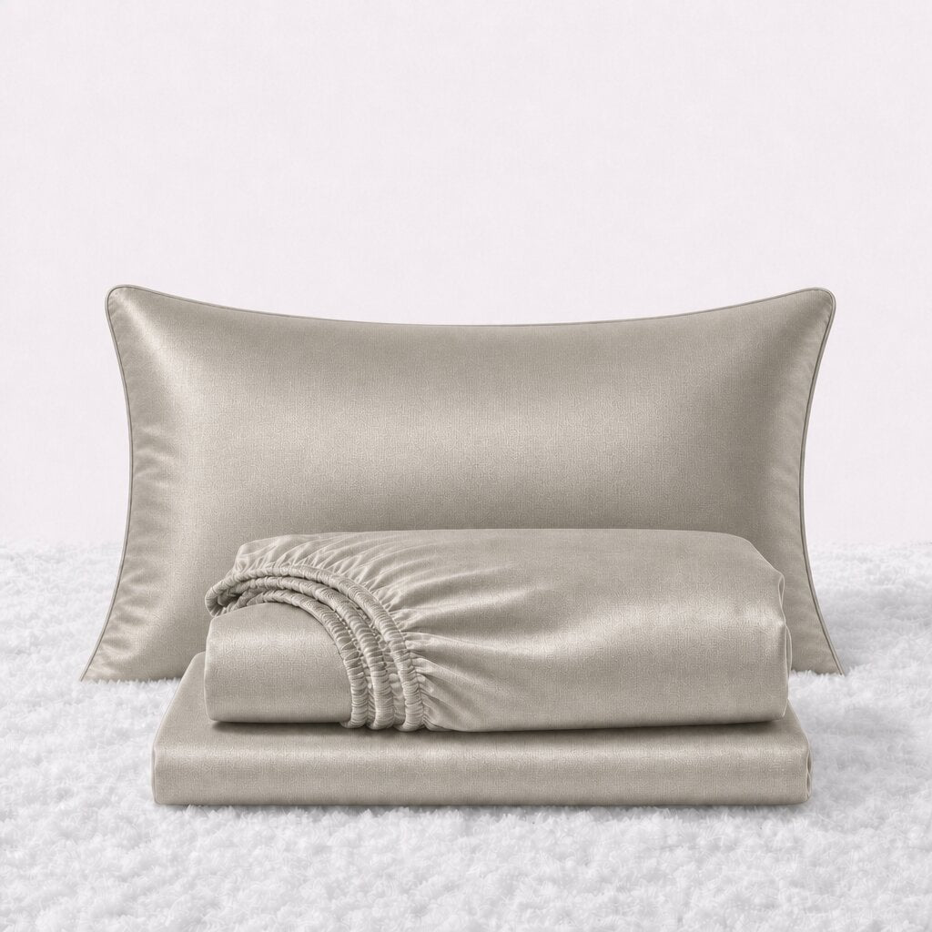 Folded shiny ivory satin sheets in front of one matching pillow on a white textured surface.