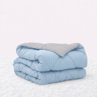 Folded light blue quilted comforter with the light gray reverse turned back, on a white textured surface.