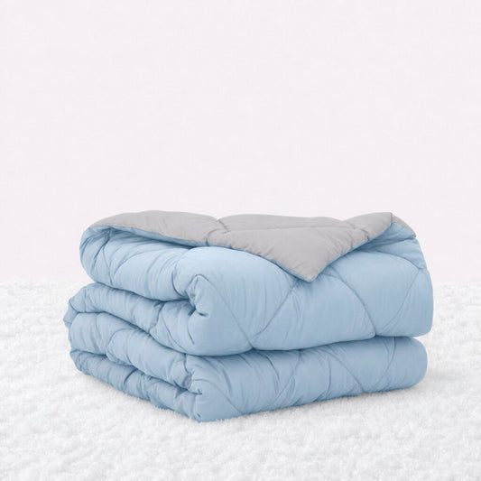 Folded light blue quilted comforter with the light gray reverse turned back, on a white textured surface.
