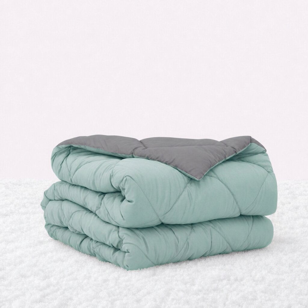 Folded mint green quilted comforter with the gray reverse turned back, on a white textured surface.