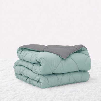 Folded mint green quilted comforter with the gray reverse turned back, on a white textured surface.