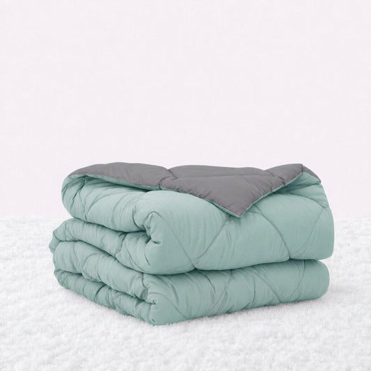Folded mint green quilted comforter with the gray reverse turned back, on a white textured surface.