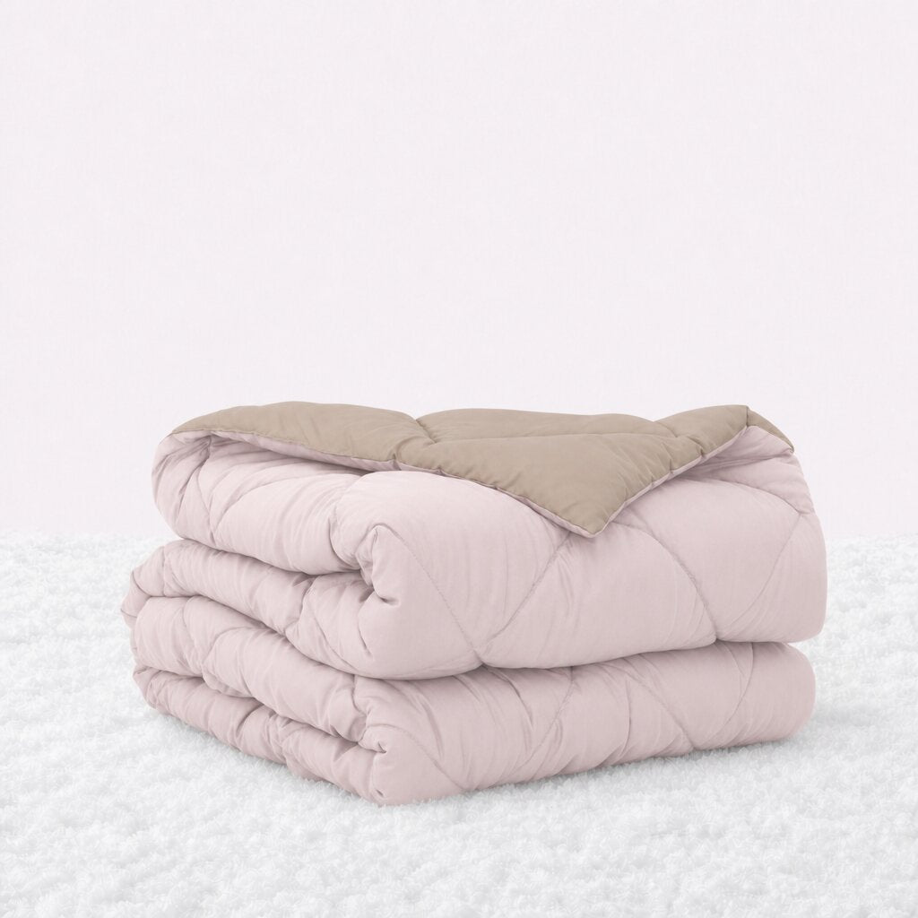 Folded blush pink quilted comforter with the tan reverse turned back, on a white textured surface.