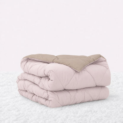 Folded blush pink quilted comforter with the tan reverse turned back, on a white textured surface.