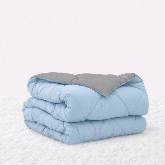 Folded light blue quilted comforter with the gray reverse turned back, on a white textured surface.