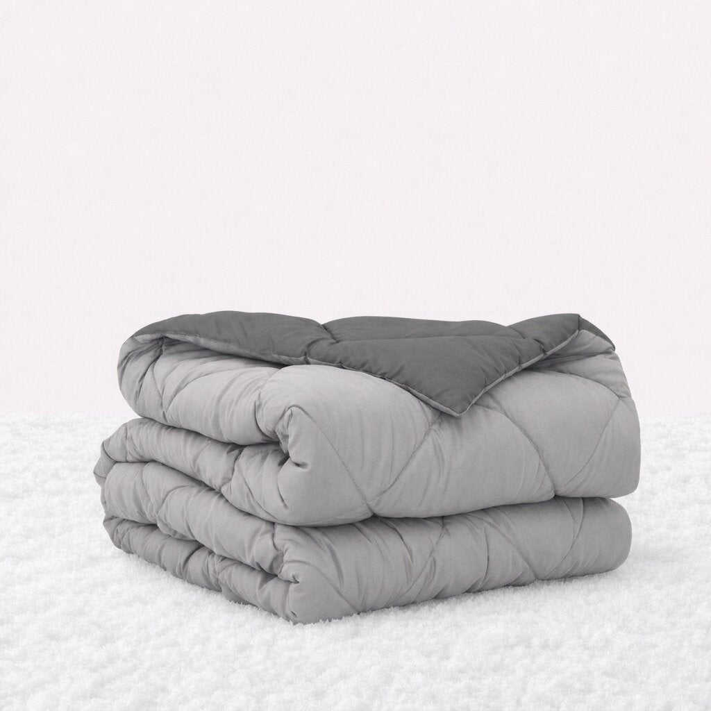 Folded light gray quilted comforter with the dark gray reverse turned back, on a white textured surface.