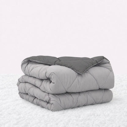 Folded light gray quilted comforter with the dark gray reverse turned back, on a white textured surface.