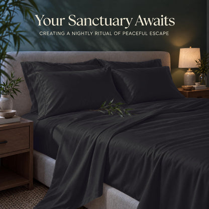 Dark gray sheets and matching pillows on a bed beside a lamp, beneath the heading "Your Sanctuary Awaits".