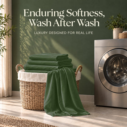 Folded forest green sheets on a wicker basket beside a washing machine, with the words "Enduring Softness, Wash After Wash".