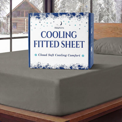 Sleephoria Cooling Fitted Sheet box standing on a warm gray fitted sheet, with matching pillows and snowy trees outside.