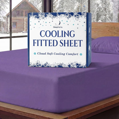 Sleephoria Cooling Fitted Sheet box standing on a purple fitted sheet, with matching pillows and snowy trees outside.