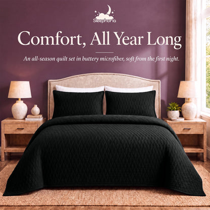 Black diamond quilt and matching shams on a bed between wooden nightstands beneath "Comfort, All Year Long".