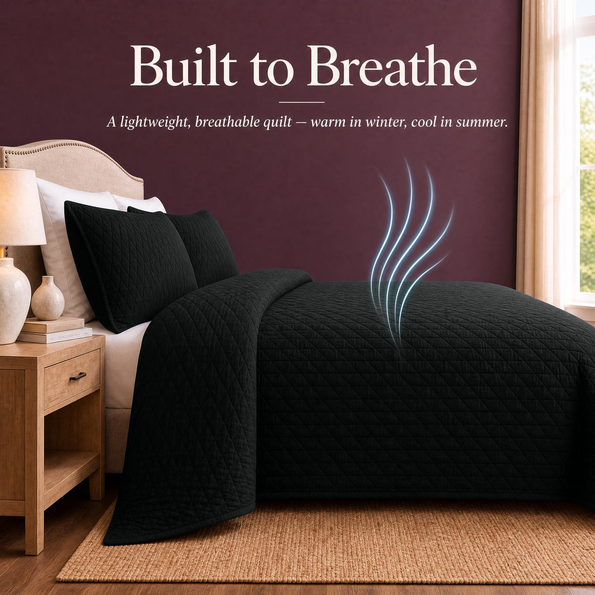 Black quilt and shams on a bed with blue airflow lines above the cover beneath "Built to Breathe".