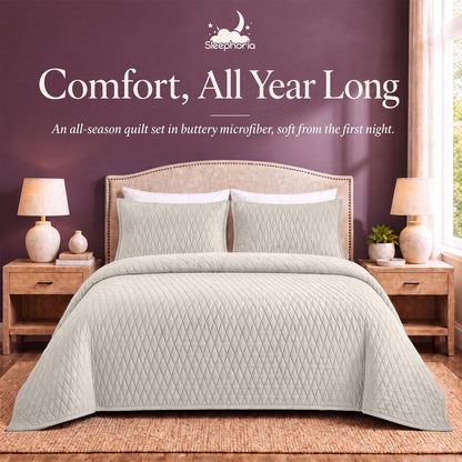Ivory diamond quilt and matching shams on a bed between wooden nightstands beneath "Comfort, All Year Long".