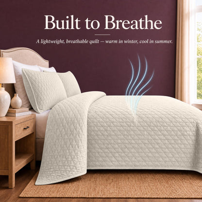 Ivory quilt and shams on a bed with blue airflow lines above the cover beneath "Built to Breathe".