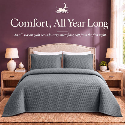 Gray diamond quilt and matching shams on a bed between wooden nightstands beneath "Comfort, All Year Long".