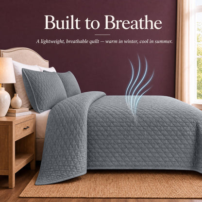 Gray quilt and shams on a bed with blue airflow lines above the cover beneath "Built to Breathe".