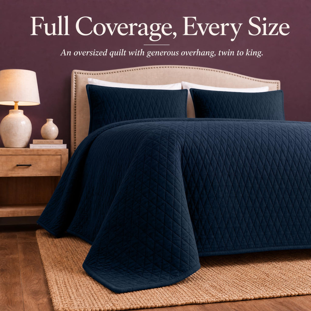 Navy blue diamond quilt draped over both sides and the foot of a bed with matching shams beneath "Full Coverage, Every Size".