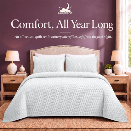White diamond quilt and matching shams on a bed between wooden nightstands beneath "Comfort, All Year Long".