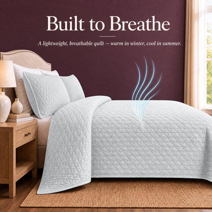 White quilt and shams on a bed with blue airflow lines above the cover beneath "Built to Breathe".